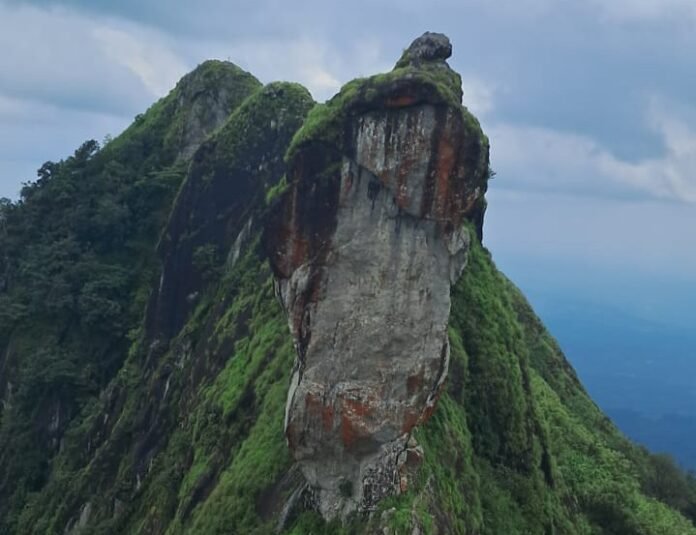 Illikkal Kallu covered in rain and mist, surrounded by lush green hills and a beautiful natural landscape.